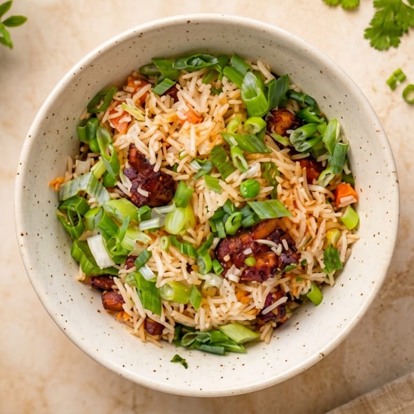 Overhead view of a bowl of fried rice with chicken, peas, carrots, and green onions.