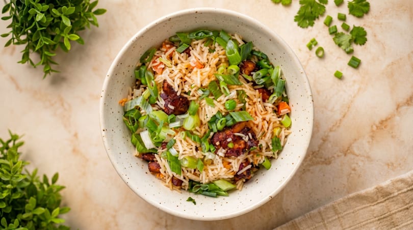 Overhead view of a bowl of fried rice with chicken, peas, carrots, and green onions.